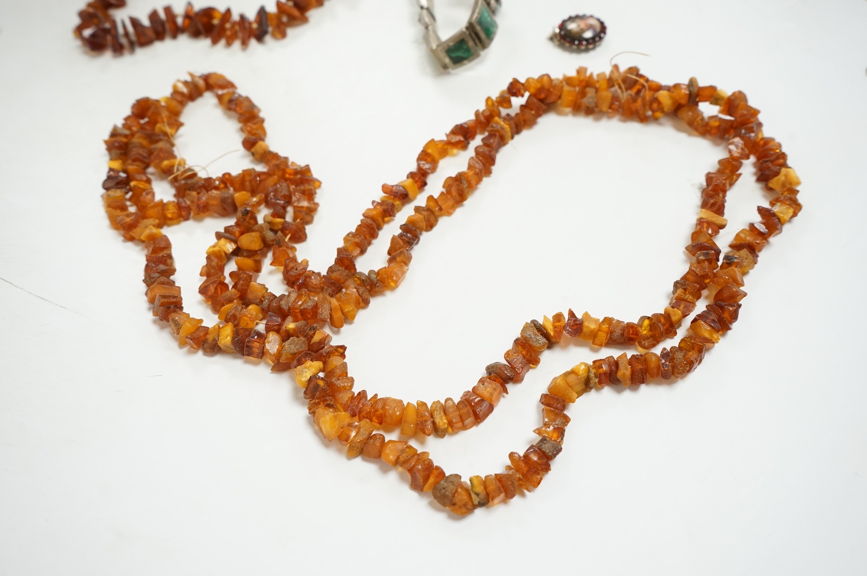 An early to mid 20th century engraved white metal and malachite set 'knot' bracelet, together with a Victorian garnet and enamel portrait pendant, a mounted jadeite disc pendant and two amber necklaces.